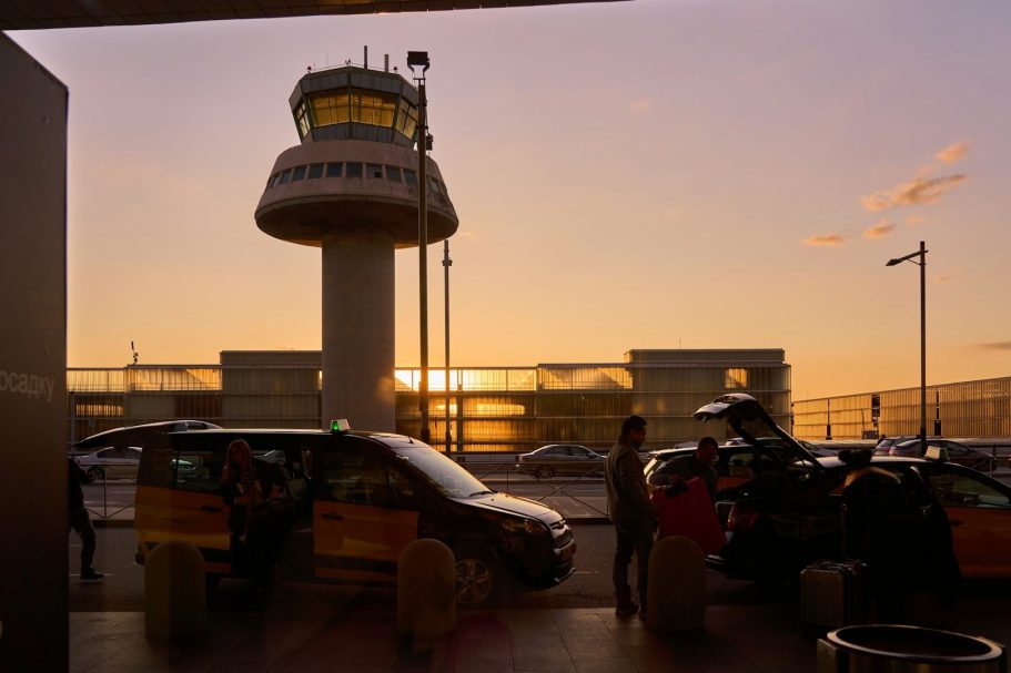 Silhouette of an airport control tower at sunset with taxis nearby.