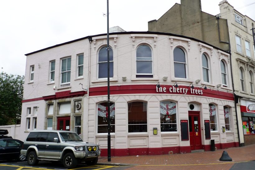 Light pink pub with red detailing, located on a corner, featuring large windows.