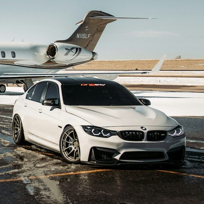 A sleek white BMW parked beside a private jet on a tarmac.