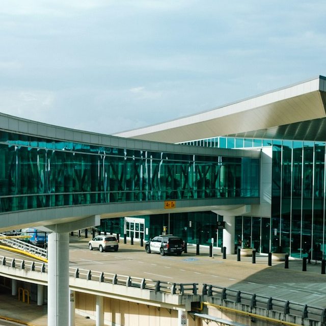 Modern airport terminal with a glass walkway and parked vehicles.