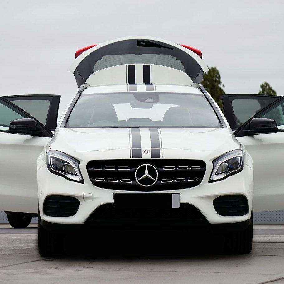 A white Mercedes car with open doors and black racing stripes.