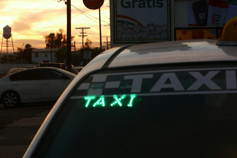 Taxi sign illuminated on top of a vehicle, with a sunset in the background.