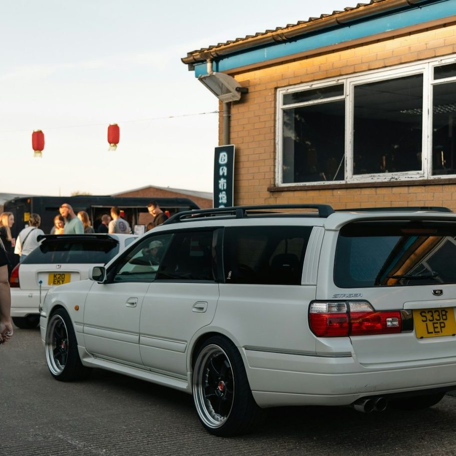 Two white cars were parked outside a building with a gathering of people nearby.