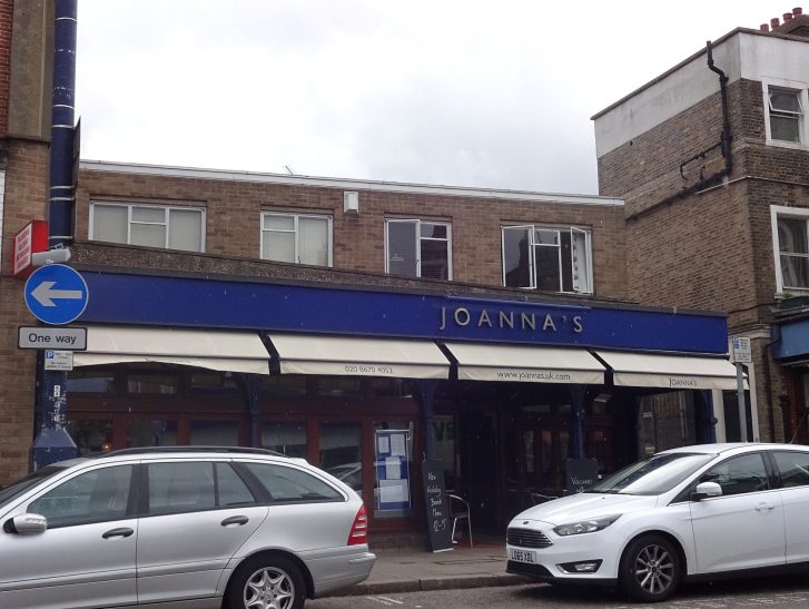 A street view of a shop with blue signage and parked cars in front.