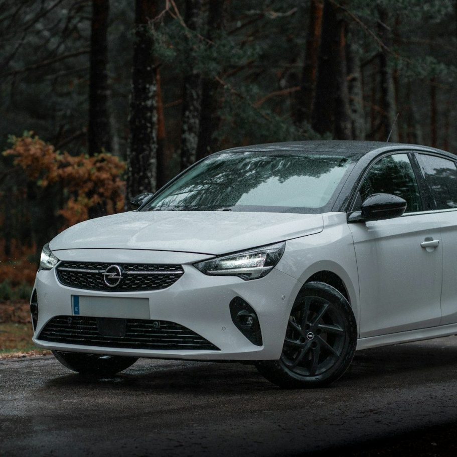 White compact car parked on a forest road surrounded by trees.