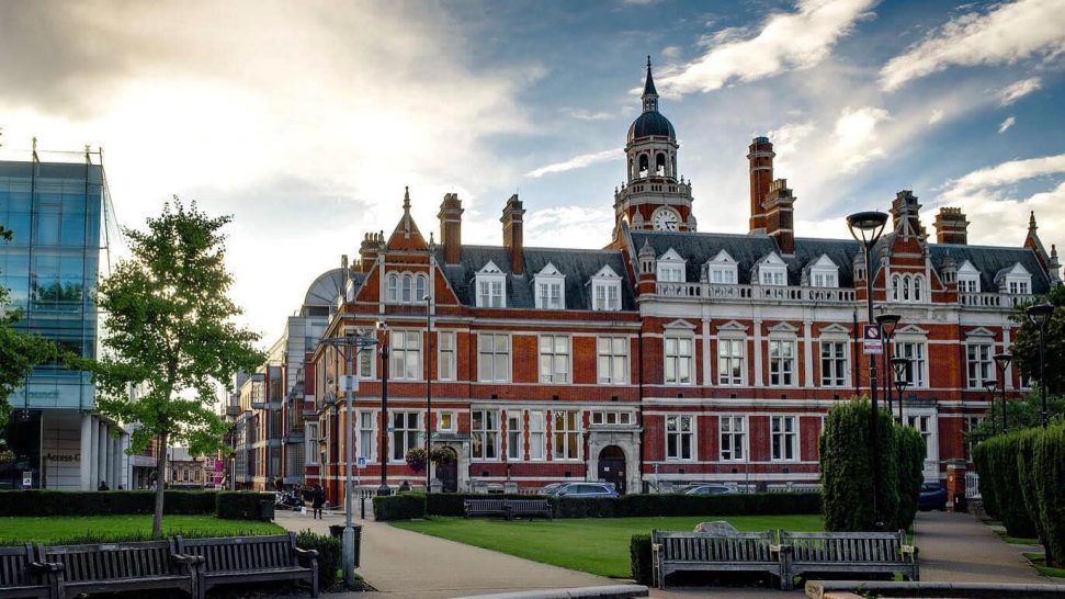 Historic building with red brick and a clock tower, set against a cloudy sky.