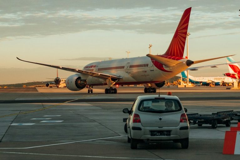 Airplane parked at the airport with a car in the foreground and another plane in the background.